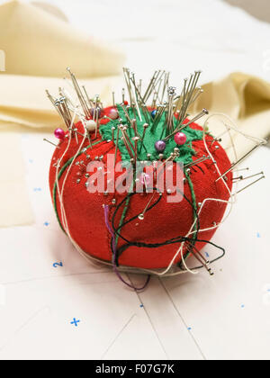 Nadelkissen in Form einer roten Tomate wird gefüllt Mit Nadeln und Nadeln Stockfoto