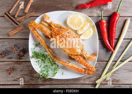 Ansicht von oben gekocht heiß und würzig Soße blaue Krabbe auf weißen Teller mit Zutaten, bei Holz Hintergrund. Frisch kochen mit heißen Stockfoto