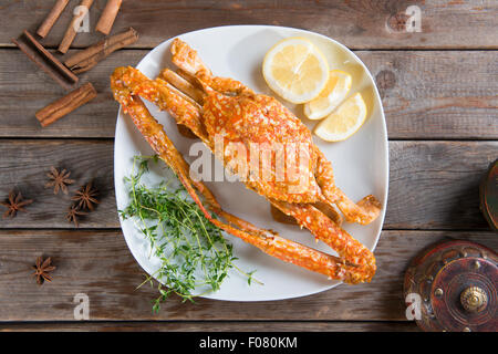 Ansicht von oben gekocht heiß und würzig Soße blaue Krabbe auf weißen Teller mit Kraut Inhaltsstoffe, bei Holz Hintergrund. Frisch kochen Witz Stockfoto