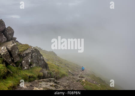 Einsamer Wanderer absteigend zu einem Nebelhaften col auf der Kentmere Hufeisen zu Fuß in Richtung Thornthwaite Crag wie der Nebel beginnt sich zu heben Stockfoto