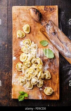 Hausgemachte rohe Tortellini und Basilikum Blätter auf dunklem Holz Stockfoto