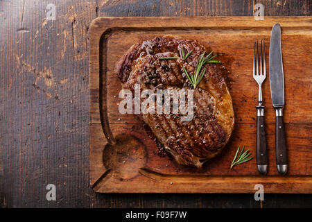 Gegrillte Black Angus Steak Ribeye und Gabel und Messer auf Fleisch Schneidbrett auf dunklem Holz Stockfoto