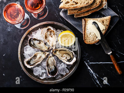 Geöffnete Austern auf Metallplatte, Brot mit Butter und Rosé auf dunklem Marmor Stockfoto