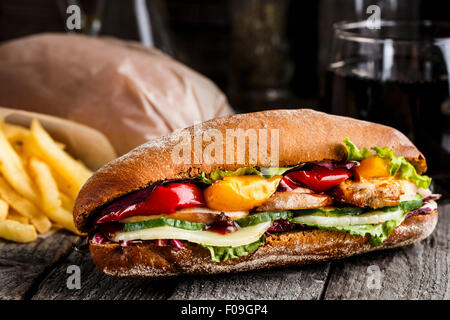 Sandwich mit Huhn, Pommes Frites und Glas Soda auf einem rustikalen Tisch Stockfoto