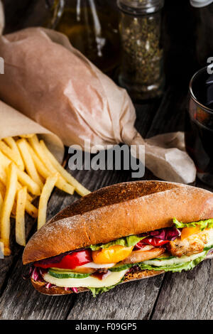 Sandwich mit Huhn, Pommes Frites und Glas Soda auf einem rustikalen Tisch Stockfoto