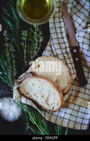 In Scheiben frisch gebackenes Ciabatta Brot mit Salz, Oregano, Olivenöl und Kräutern Thym. Auf weißen überprüft Küchentuch mit Messer ove Stockfoto