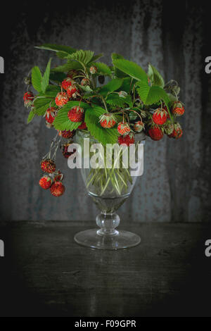 Haufen von reifen Walderdbeeren mit Blättern in Vintage Glas über alte Metall Hintergrund. Rustikalen Stil. Natürliches Tageslicht. Stockfoto