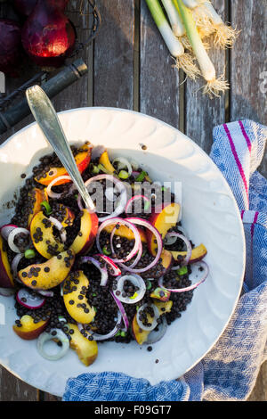 Schüssel mit Linsen und Obstsalat auf einem hölzernen Gartentisch mit Küchentuch. Ansicht von oben Stockfoto