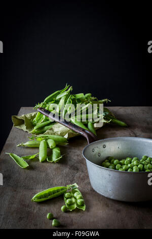 Erbsen in Vintage Sieb und Pods auf Papiertüte auf Holztisch Stockfoto