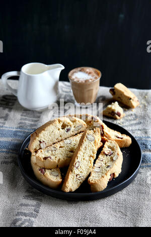 Mandel italienische Biscotti auf einem Teller mit einem Glas Kaffee und einen Krug Milch im Hintergrund Stockfoto