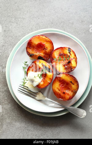 Platte mit Gegrillter Pfirsich mit griechischer Joghurt, Honig und dekoriert mit frischem Thymian Stockfoto