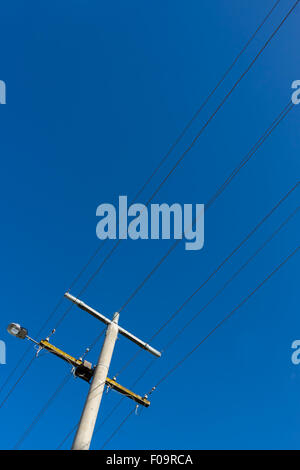 Strommast und Stromleitungen mit einer Straße leuchtet am blauen Himmel. Stockfoto