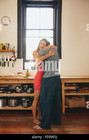Junges Liebespaar umarmt einander zu Hause in der Küche - drinnen erschossen Stockfoto