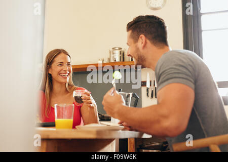 Glückliches junges Paar zu Hause frühstücken. Junge Frau trinkt Kaffee und Man beim Sitzen am Tisch gruppenweise Frühstück Essen Stockfoto