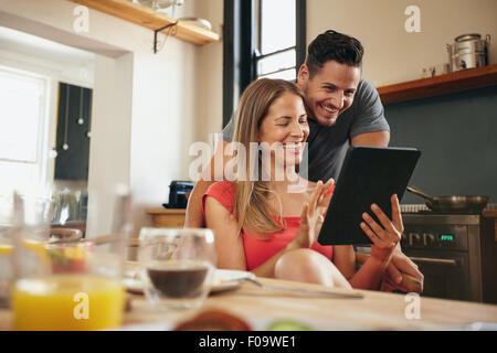 Glückliches junges Paar in der modernen Küche am Morgen mit einem digitalen Tablet. Lächelnde junge Frau zeigen etwas auf ihr bo