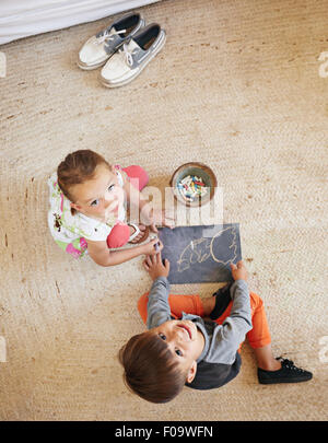 Draufsicht der zwei kleine Kinder sitzen am Boden nach oben auf die Kamera während des Zeichnens. Stockfoto