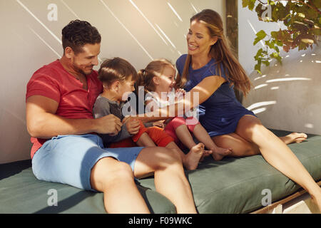 Schuss der glückliche junge Familie Zusammensitzen im Patio. Paar mit ihren Kindern sitzen auf der Couch im Hinterhof Spaß. Stockfoto