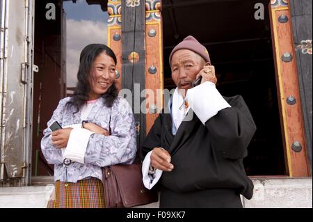 Mann am Telefon während die Frau neben ihm stehen und Lächeln, Bhutan Stockfoto