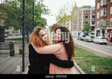 Im Freien Schuss von zwei Freundinnen, die zu Fuß durch die Stadt mit Blick auf die Schulter lächelnd. Glückliche junge Frauen zusammen spazieren entlang einer c Stockfoto