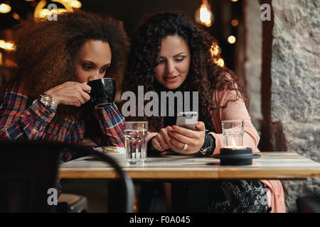 Junge Freunde sitzen in einem Café, ein Smartphone zu betrachten. Eine Frau Kaffee trinken und ein anderes Mobiltelefon zu halten, Stockfoto