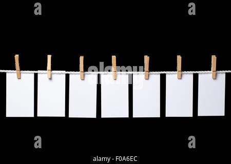 Bild von sieben kleinen weißen Papierbögen mit Wäscheklammern am Seil aufgehängt. Die Zusammensetzung ist auf schwarzem Hintergrund isoliert. Die rela Stockfoto
