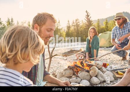 Familie sitzen um Lagerfeuer Kochen Fisch Zweig befestigt Stockfoto