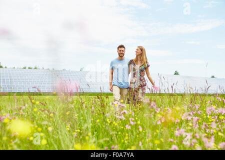 Junges Paar Spaziergang durch Feld neben Solarpark Stockfoto