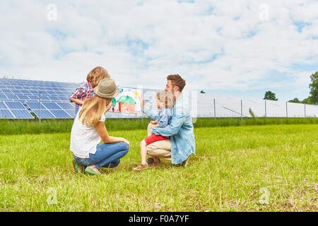 Junge Familie im Feld sitzen, mit Blick auf Kinder Zeichnung des Hauses, neben Solarpark Stockfoto