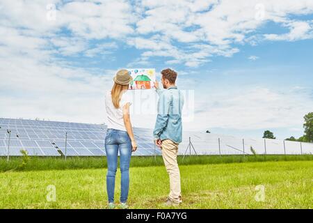 Junges Paar im Feld stehen, mit Blick auf Kinder Zeichnung des Hauses, neben Solarpark Stockfoto