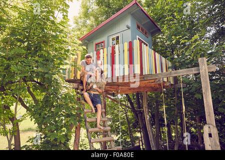 Junges Paar sitzt auf Leiter-Baumhaus Stockfoto