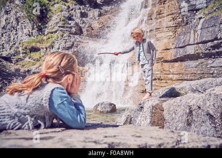 Junge Mädchen beobachten Bruder, stehend neben Wasserfall