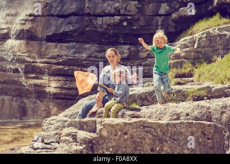 Mutter und Söhne, sitzen auf den Felsen von Wasserfall, Fischen mit Netz Stockfoto