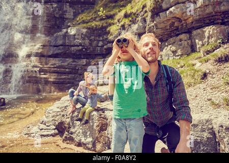 Junge Familie, die neben Wasserfall erkunden Stockfoto