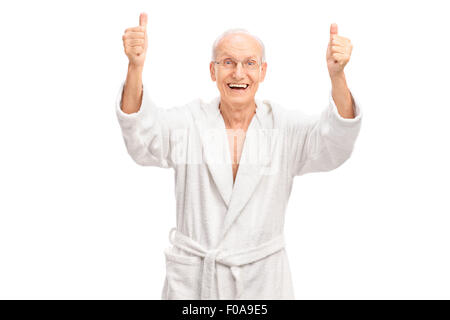 Studioaufnahme von einem überglücklich Senior in einem weißen Bademantel geben zwei Daumen nach oben und schaut in die Kamera Stockfoto