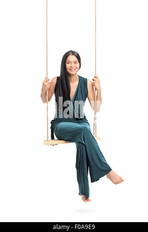 Vertikale Aufnahme einer modischen Frau sitzen auf einer Schaukel und schaut in die Kamera, die isoliert auf weißem Hintergrund Stockfoto