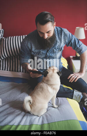 Young bärtiger Mann mit Smartphone auf Bett Stockfoto