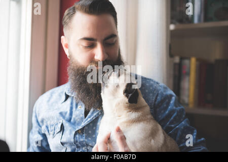 Young bärtiger Mann mit Hund auf Arm Stockfoto