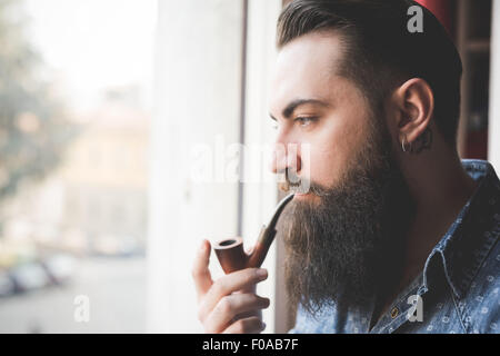 Junge bärtige Mann Pfeife durch Fenster Stockfoto