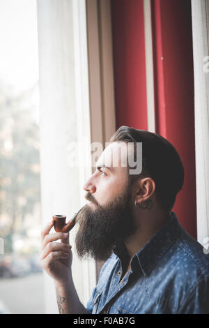 Junge bärtige Mann Pfeife durch Fenster Stockfoto