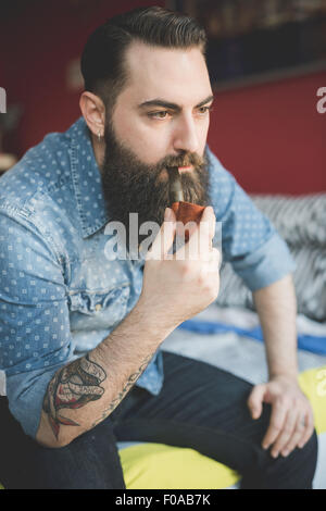 Junge bärtige Mann Pfeife auf Bett Stockfoto