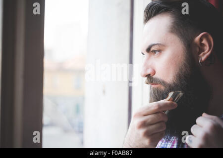 Young bärtiger Mann trimmen sein Bart durch Fenster Stockfoto