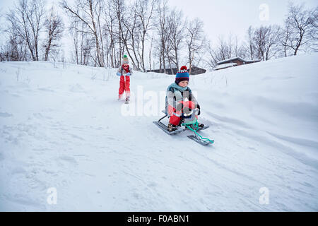 Zwei Brüder auf Schlitten und Schnee Scooter auf schneebedeckten Hügel, Hemavan, Schweden Stockfoto