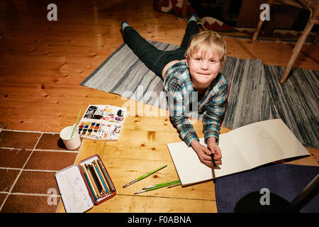 Junge liegend am Boden mit Aquarellfarben und Skizzenblock Stockfoto