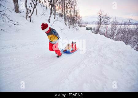 Jungen ziehen Bruder auf Schlitten Schnee bedeckt Hügel, Hemavan, Schweden Stockfoto