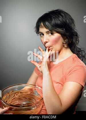 Studioaufnahme von junge Frau mit Rührschüssel Schokolade vom Finger lecken Stockfoto