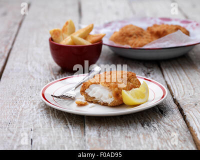 Panierte klobige Kabeljau mit Schale Pommes Frites auf Holztisch Stockfoto