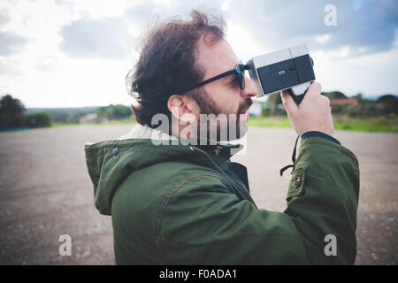 Mitte erwachsener Mann mit Vintage Filmkamera auf Brachland Stockfoto