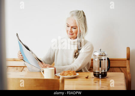 Ältere Frau liest Zeitung beim Frühstück Stockfoto