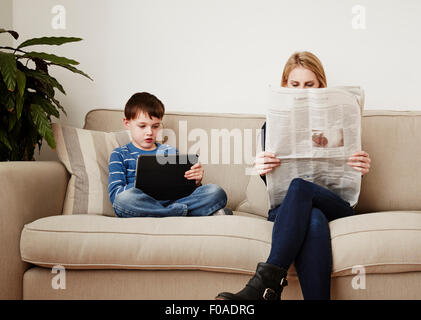 Kleiner Junge mit digital-Tablette, Mutter lesen Zeitung Stockfoto