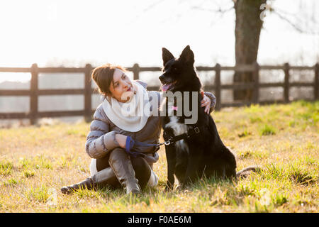 Mitte erwachsenen Frau sitzt mit ihrem Hund im Feld Stockfoto
